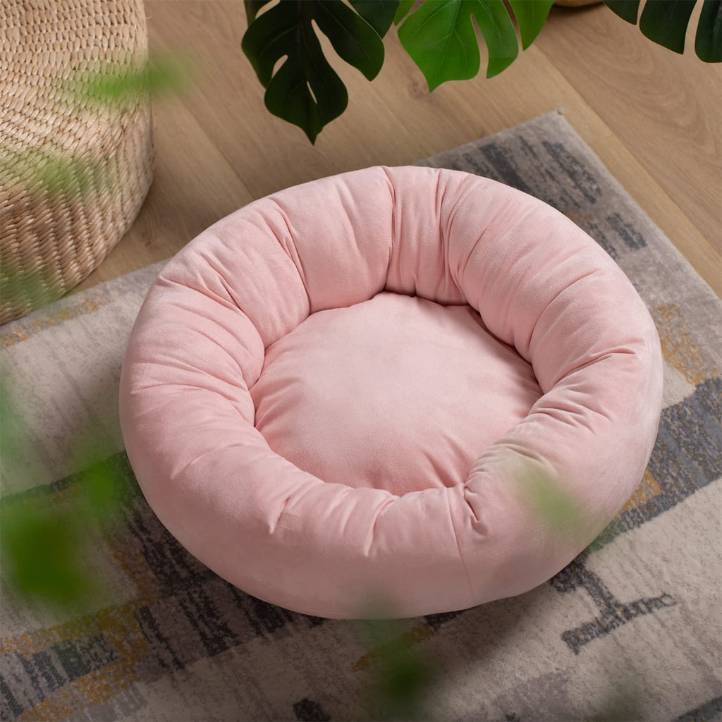 Pink round dog bed cushion with deep rim, set on a patterned rug.
