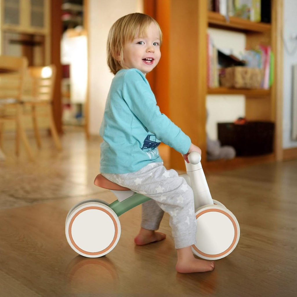 Young child pushing a toddler balance bike with green frame, orange seat, and 4 wheels