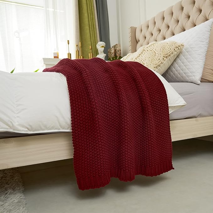 Wine red chunky cable-knit cotton throw blanket draped over a bed edge.
