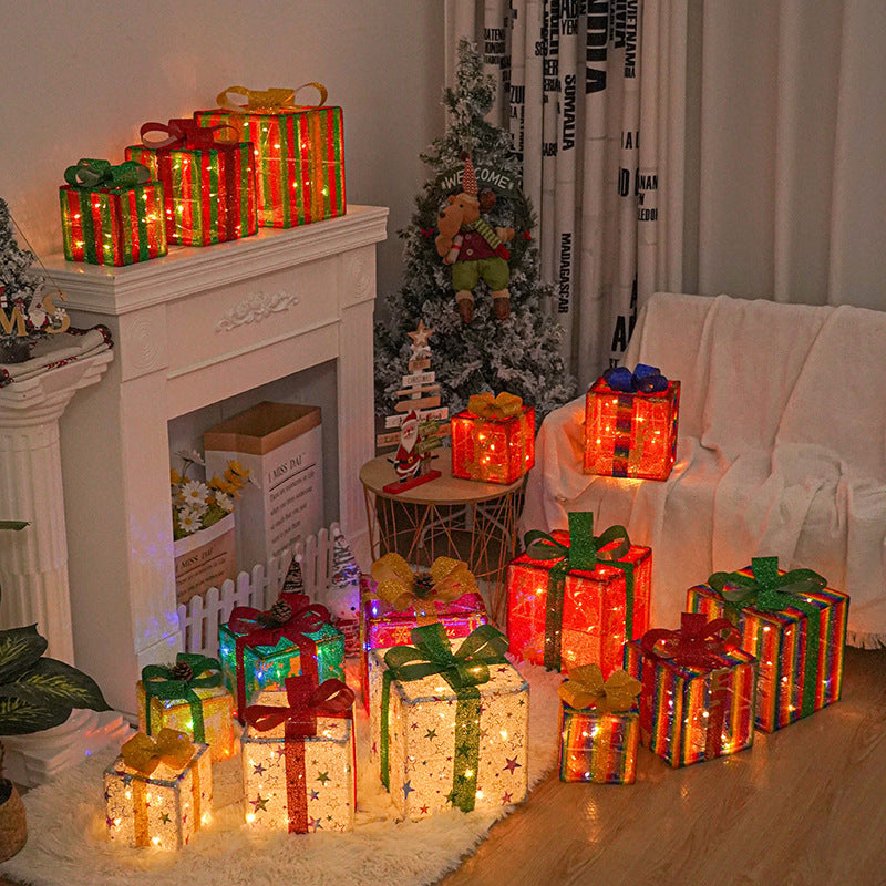 Lit set of Christmas gift boxes with red and green bows and glowing string lights