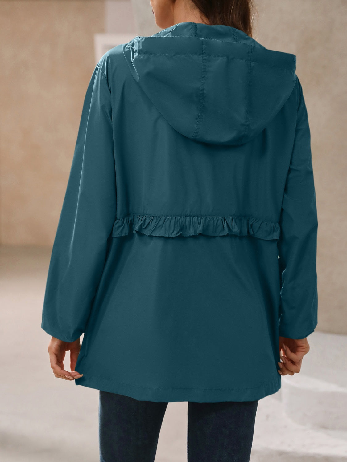 Women’s hooded windbreaker jacket back view, teal-blue with ruffle waist detail