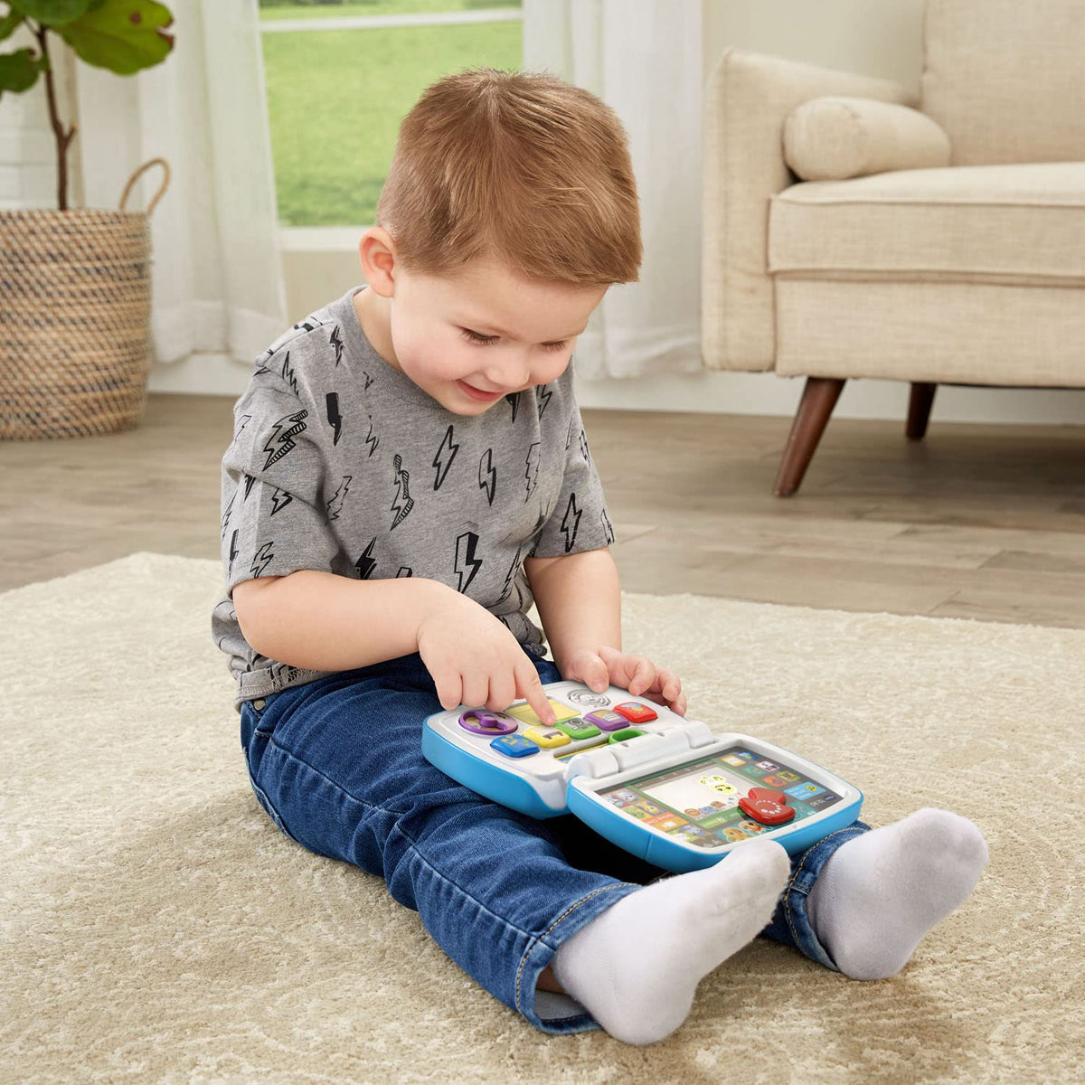 Small child seated using a blue interactive toddler laptop with control buttons and screen