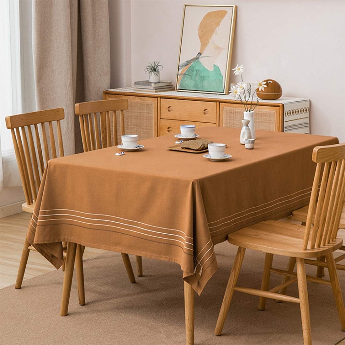 Cotton tablecloth with striped border and tassel trim on a dining table, camel-brown tone.