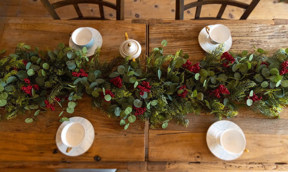 Artificial green Christmas garland with red berry clusters laid across a wooden table