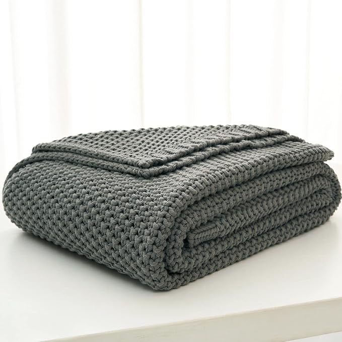 Folded chunky cable knit throw blanket in light-to-medium gray with textured rows.