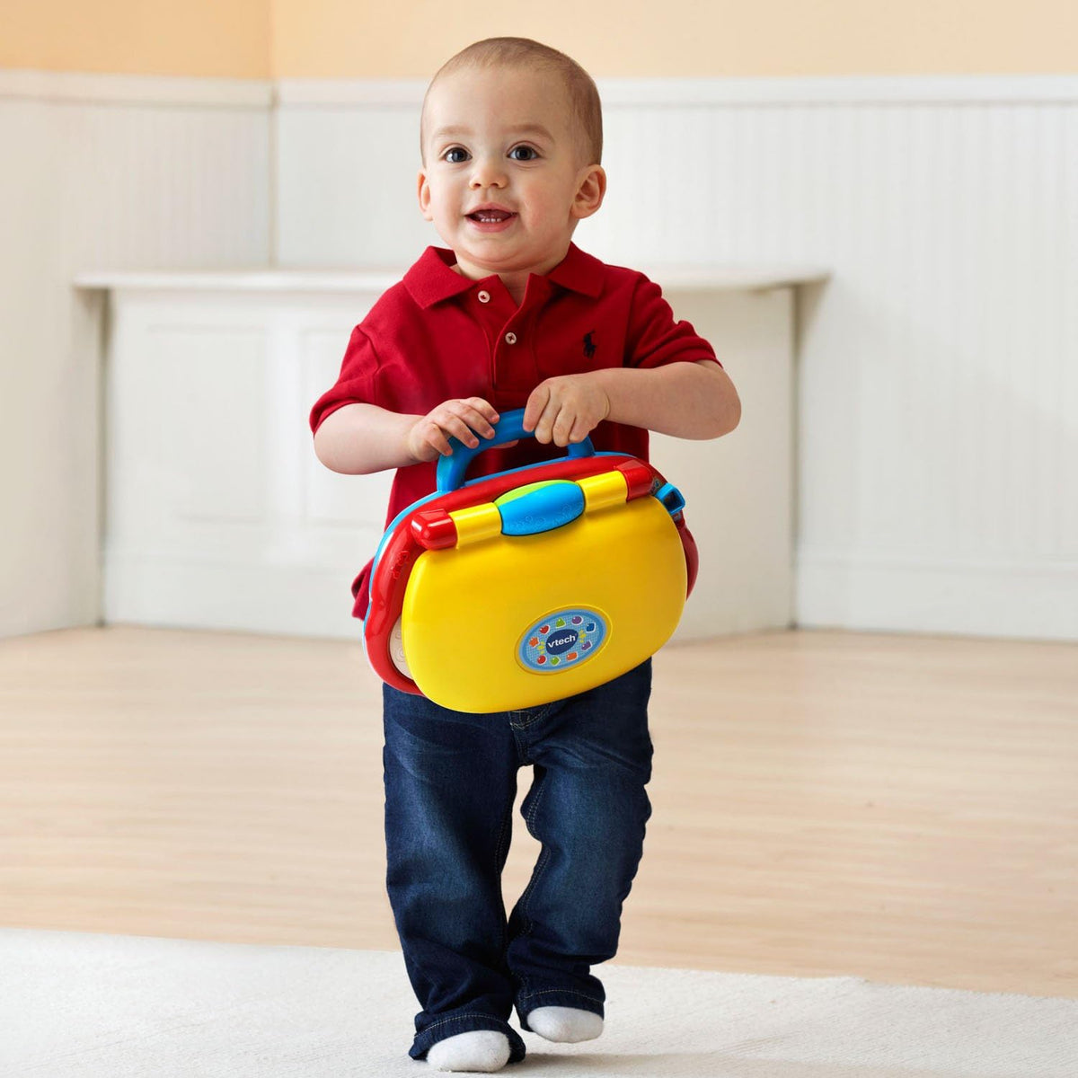 Baby standing holding a yellow-and-blue toddler tech laptop with rounded handle