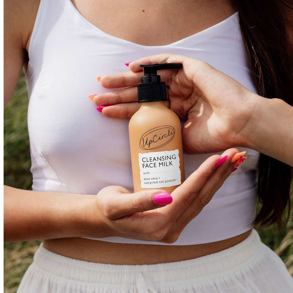 Hands pumping cleansing face milk from black dispenser onto skin