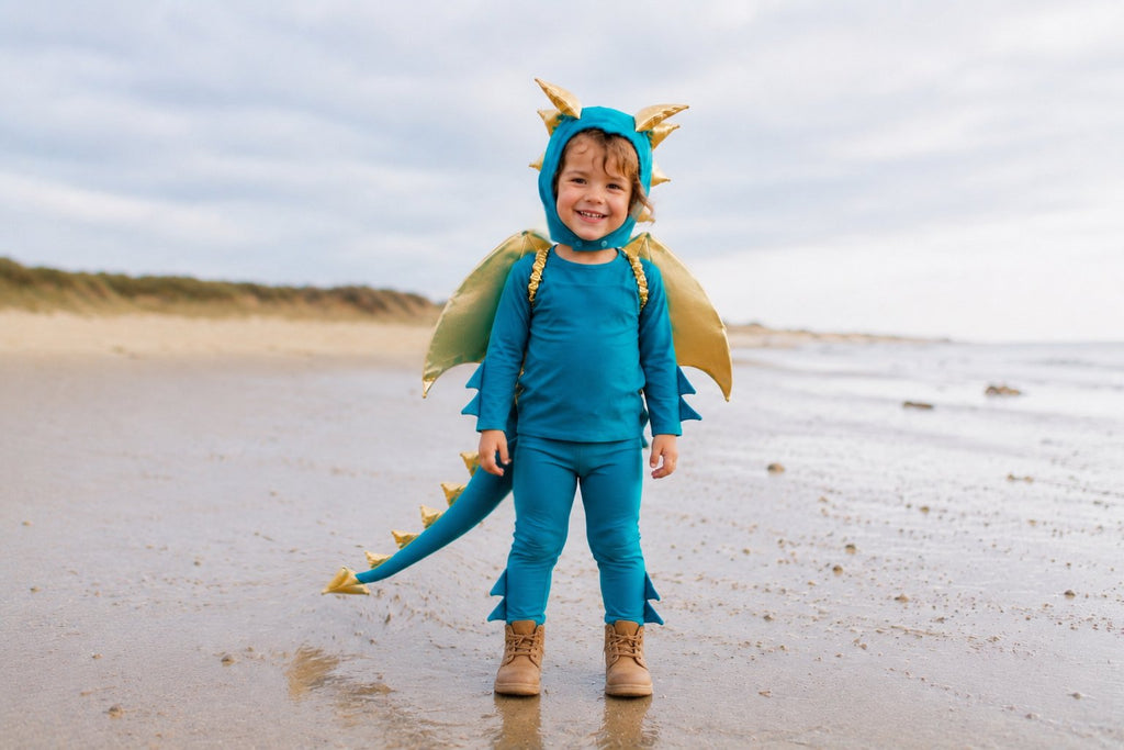 Turquoise dragon costume with gold wings and headpiece, toddler standing on beach sand.
