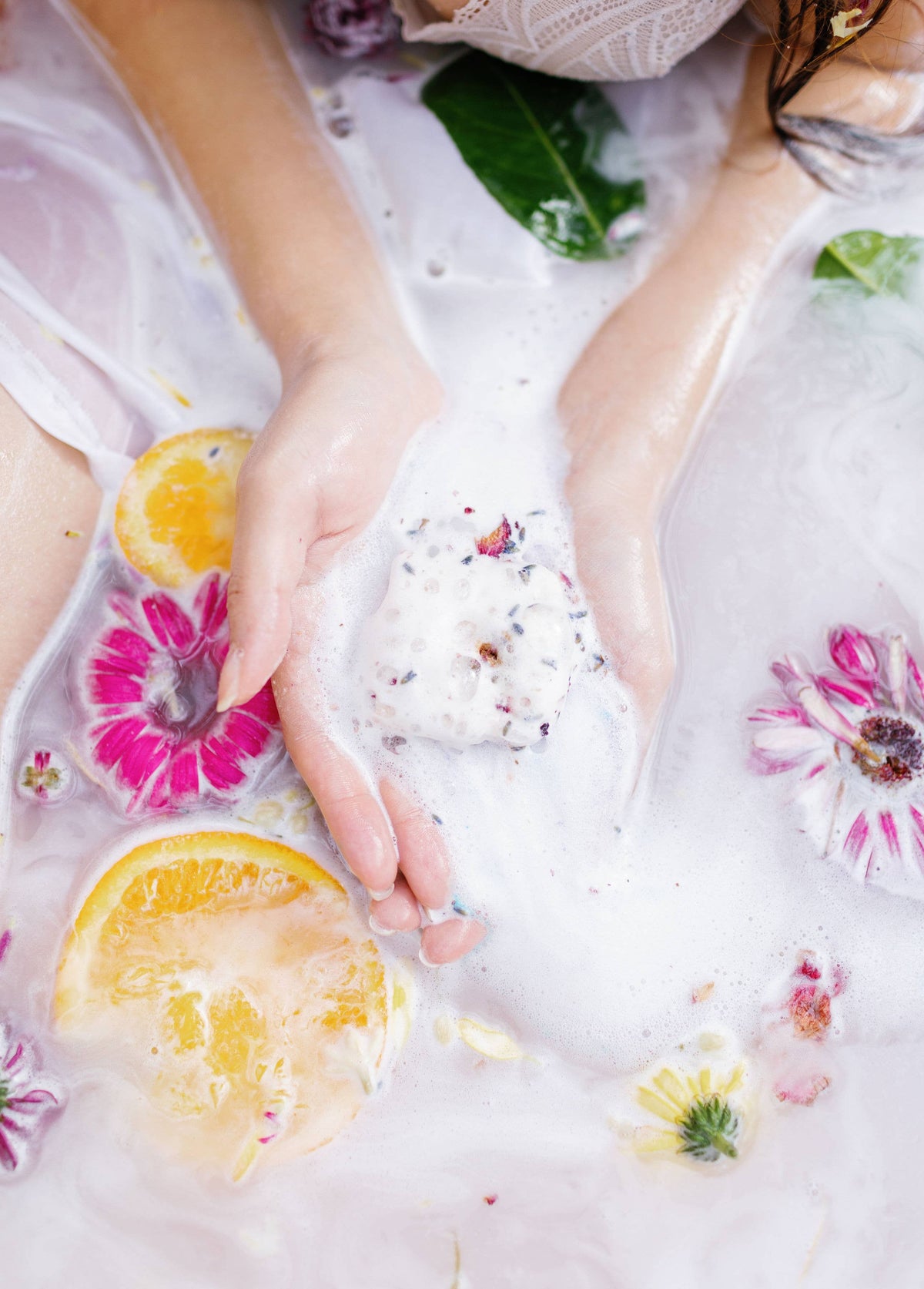 Square bath bombs floating in foamy bathwater: white cube with blue specks and yellow cube