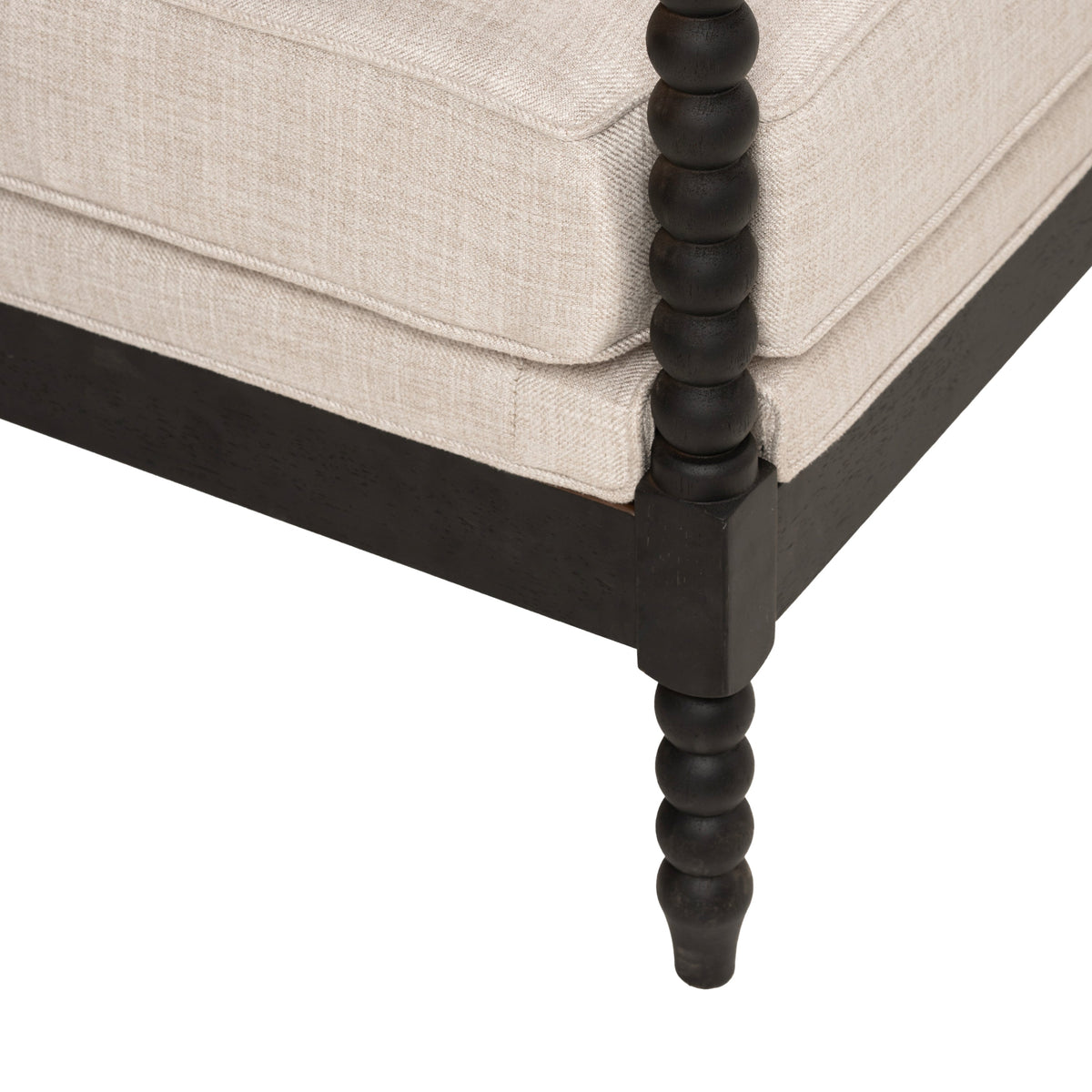 Accent chair corner showing beige upholstery, dark wood frame, and a turned bead-style leg