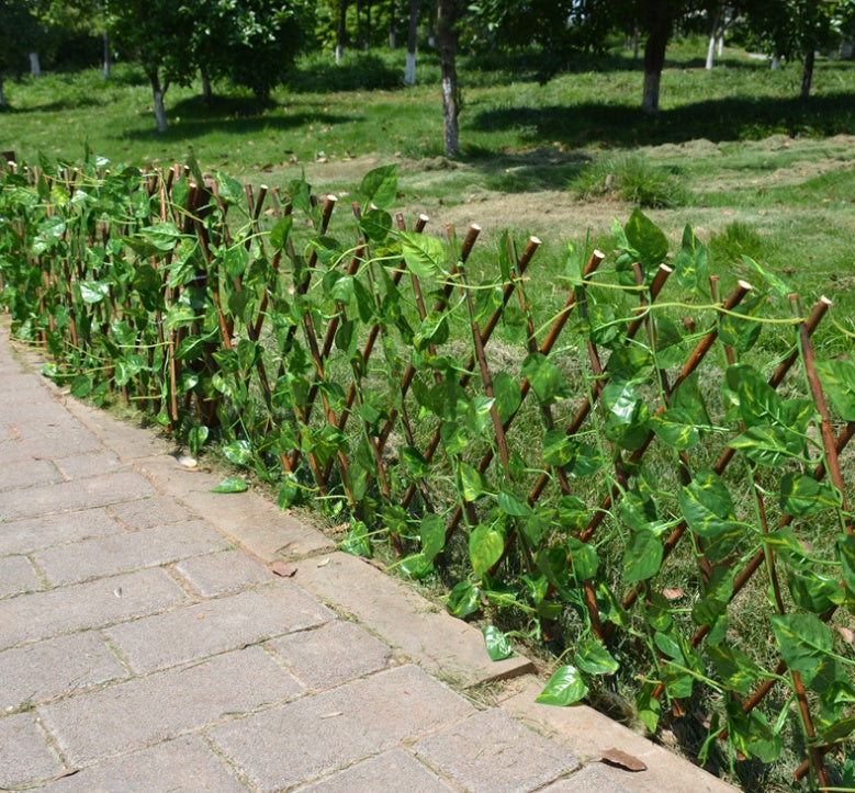 Expandable wooden plant trellis fence with dense green leaves along a paved path