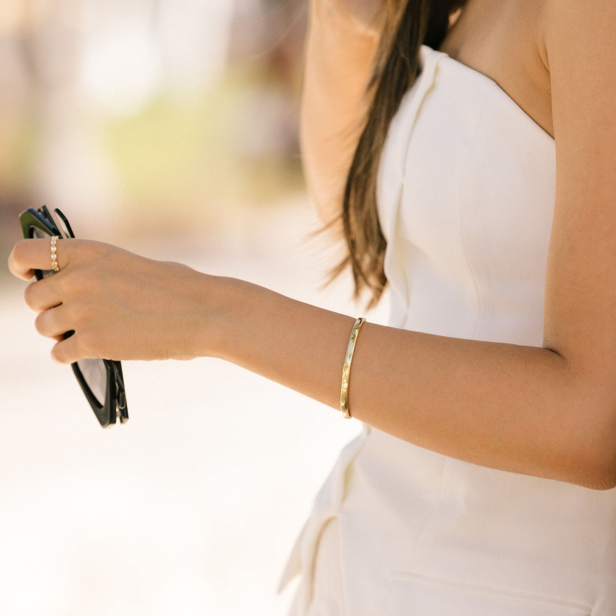 Gold-tone cuff bracelet on wrist, smooth flat design.