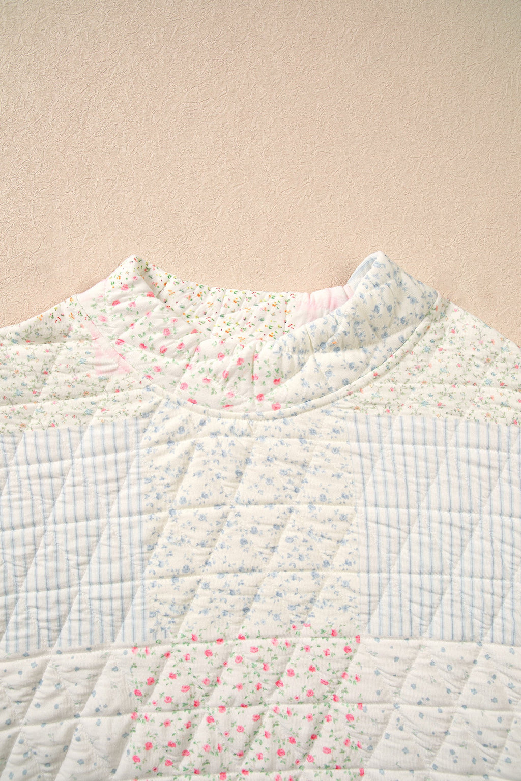 Quilted mock neck top close-up, floral patchwork, light base with pink and blue