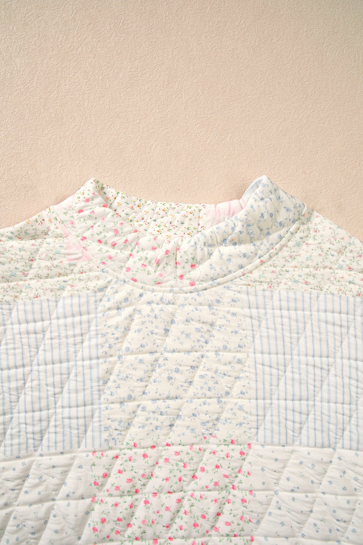 Quilted mock neck top close-up, floral patchwork, light base with pink and blue