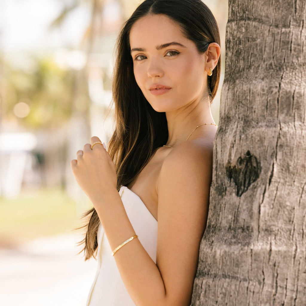 Gold-tone cuff bracelet worn with a stacked bracelet look.