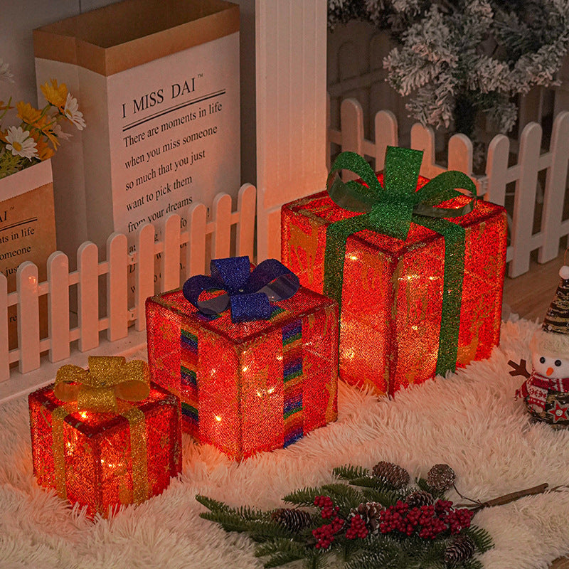 Four illuminated gift boxes with red and green bows on a tree display