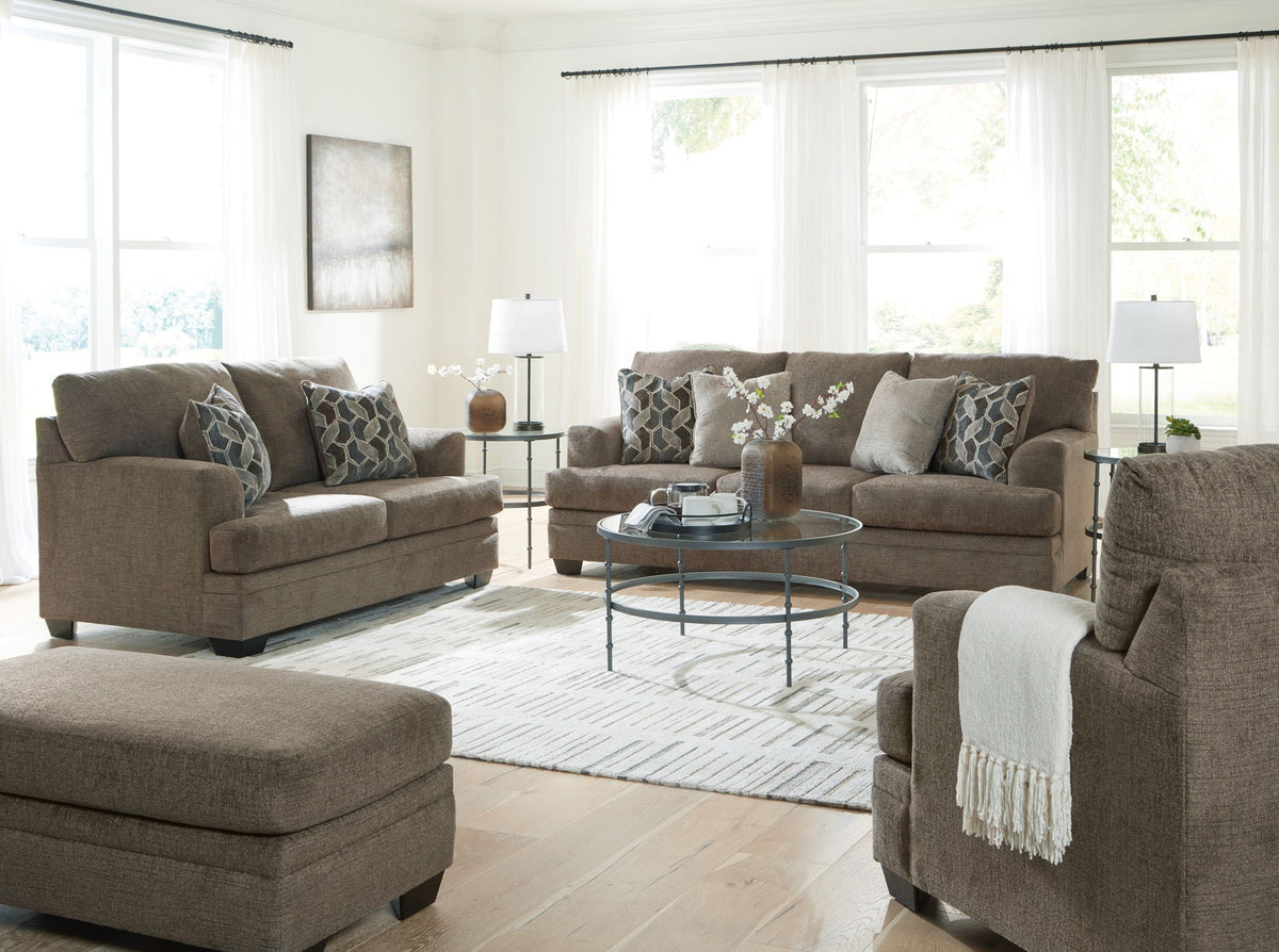 Tan fabric living room set with sofa, armchairs, and ottoman with patterned pillows