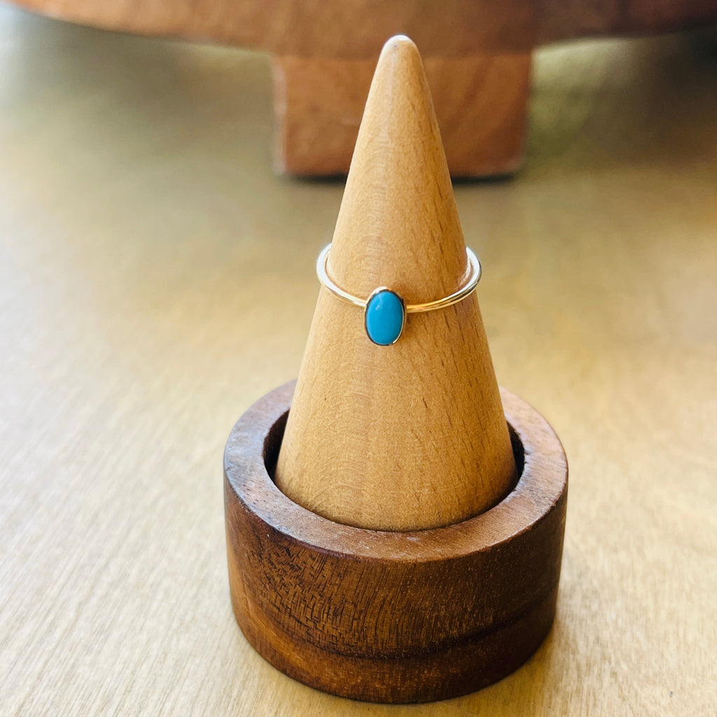 Gold-tone ring with oval turquoise cabochon on slim band, upright on a stand