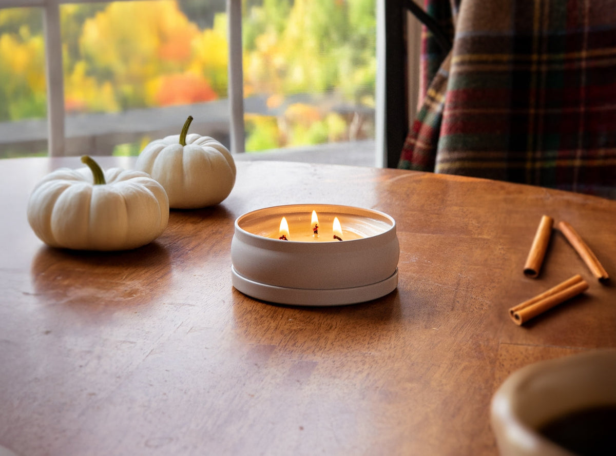 Lit white 3-wick candle in a round tin on a wooden table, with flames visible