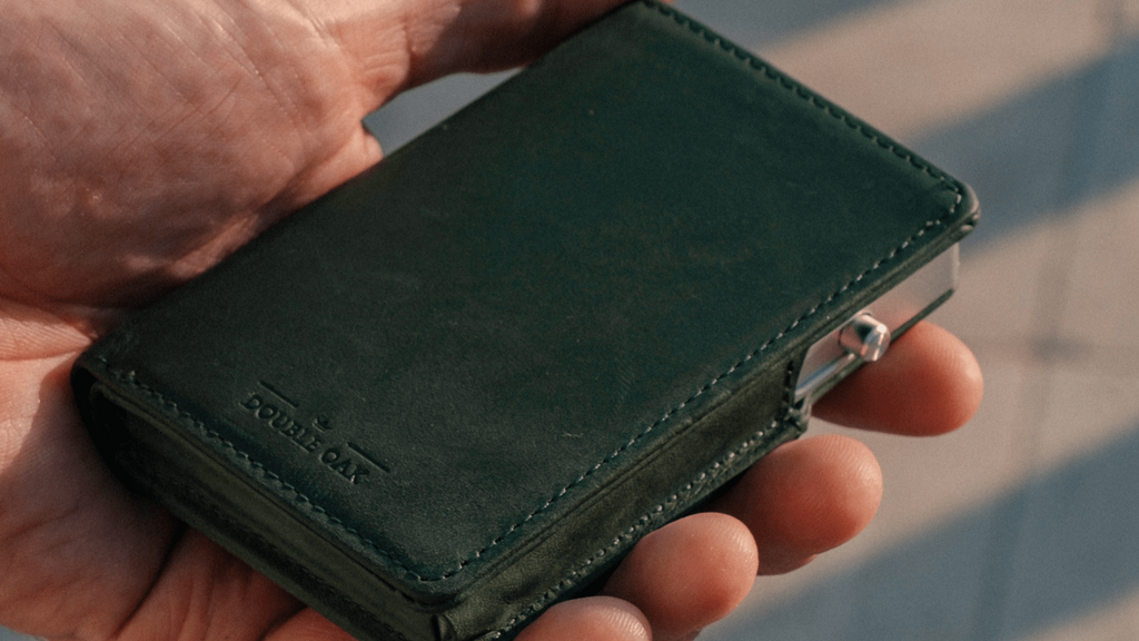 Dark green bifold wallet close-up with snap tab and embossed logo.