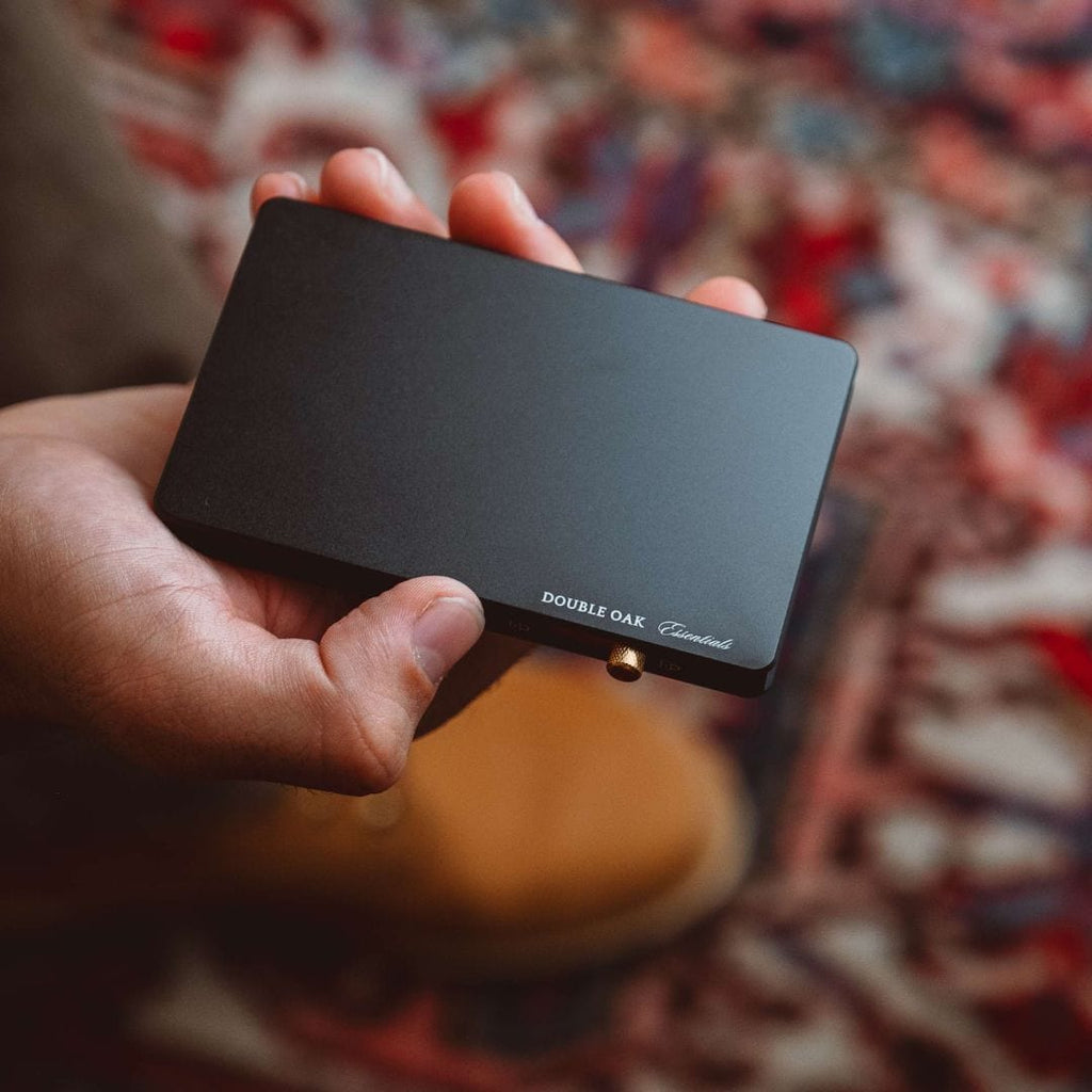 Matte black pop-up cardholder with front label and brass button closure, held in hand.