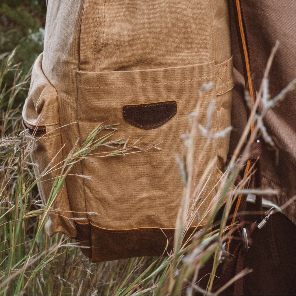 Sand waxed canvas backpack with leather emblem patch and front pocket, close-up
