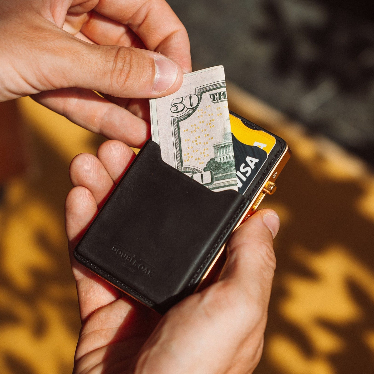 Black leather card wallet with cash insert and Visa card, held in hand