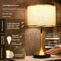 Gold table lamp with off-white fabric shade and gold base with dark round foot