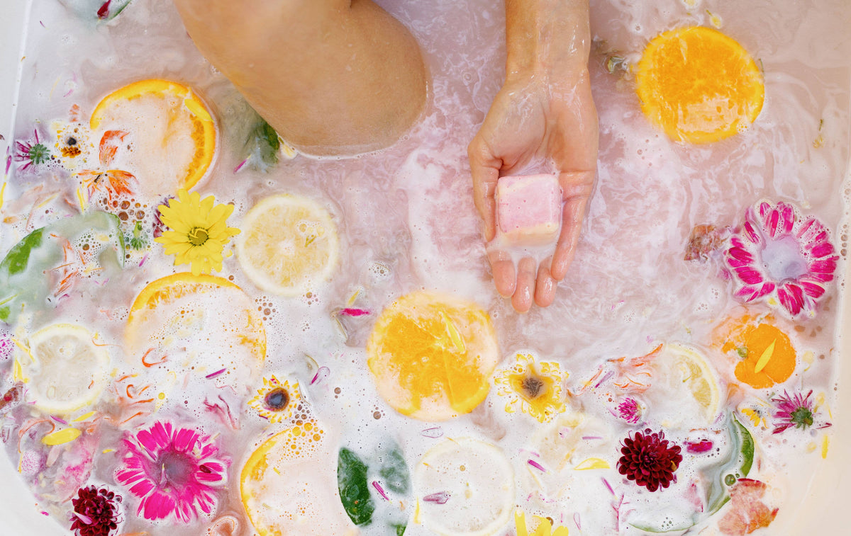 Bath bomb pieces floating in foamy water, mostly round yellow and pink, with white cubes