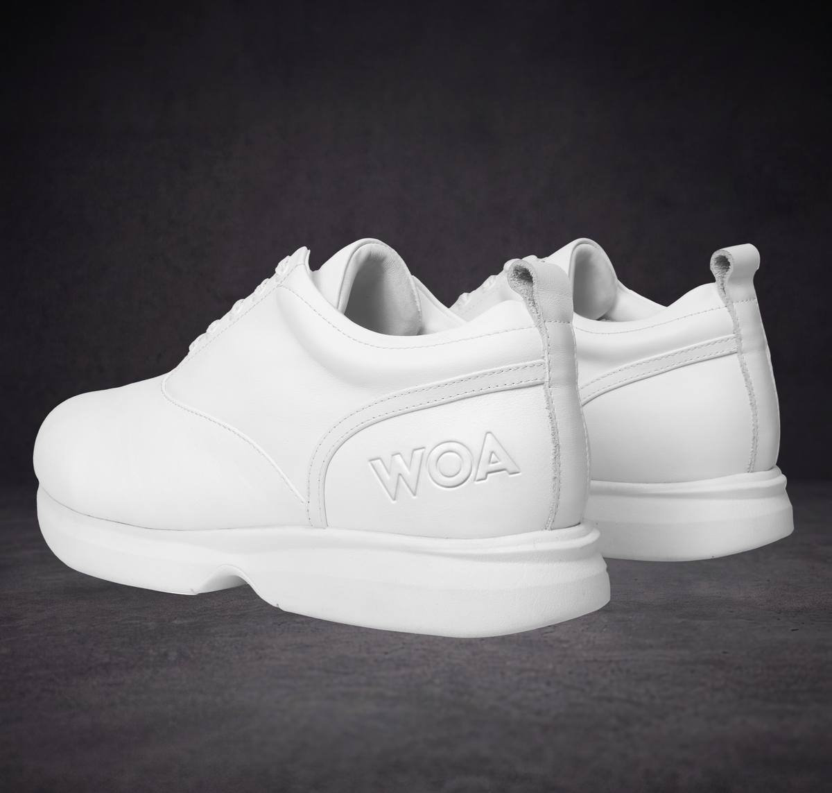 Pair of white low-top sneakers showing side profile and WOA logo