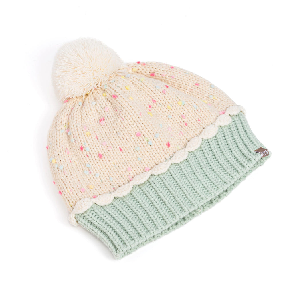 Cream pom-pom beanie with pastel sprinkles and mint ribbed cuff, angled view.
