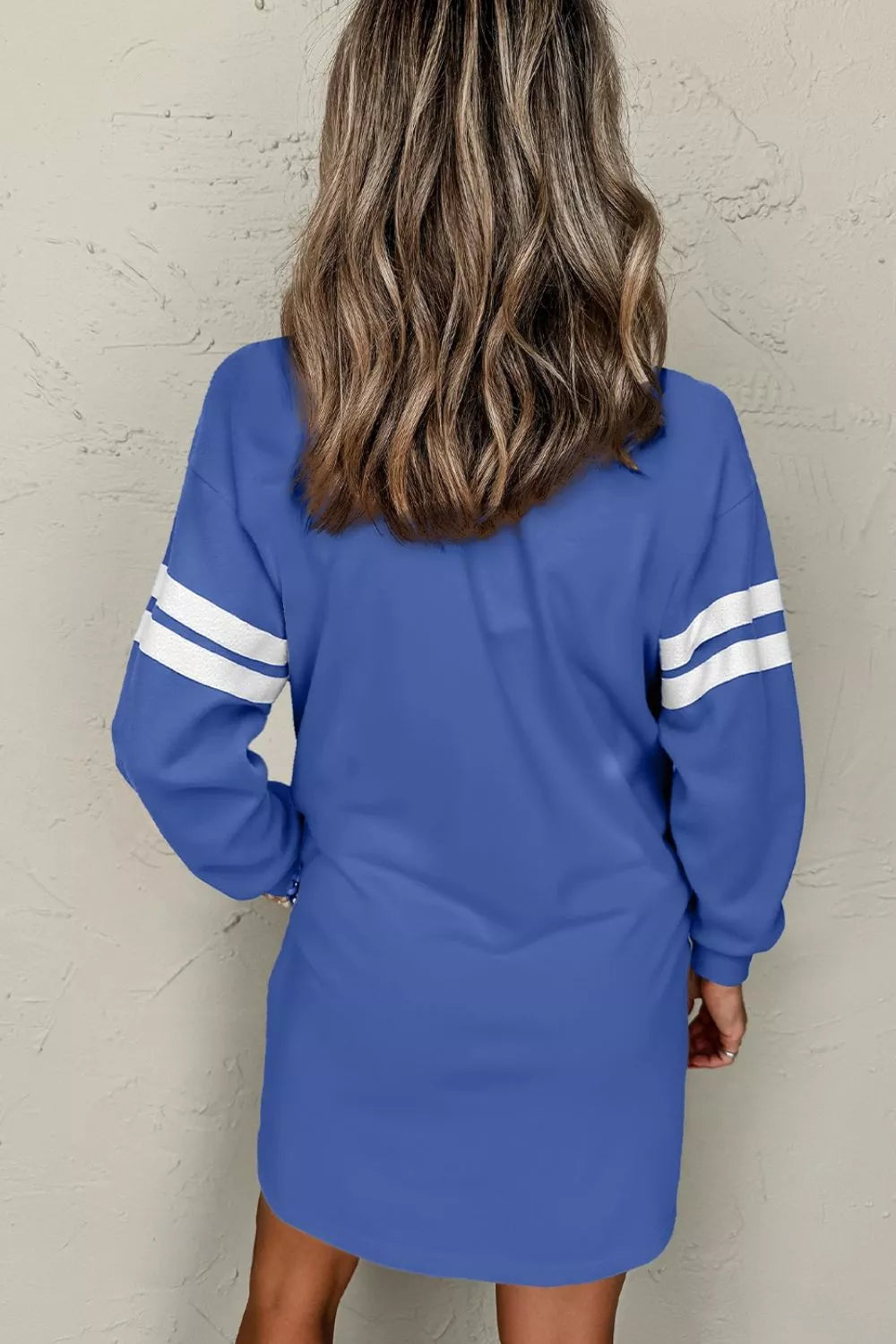 Back view of dusty blue sweatshirt dress with white striped sleeves and relaxed fit.
