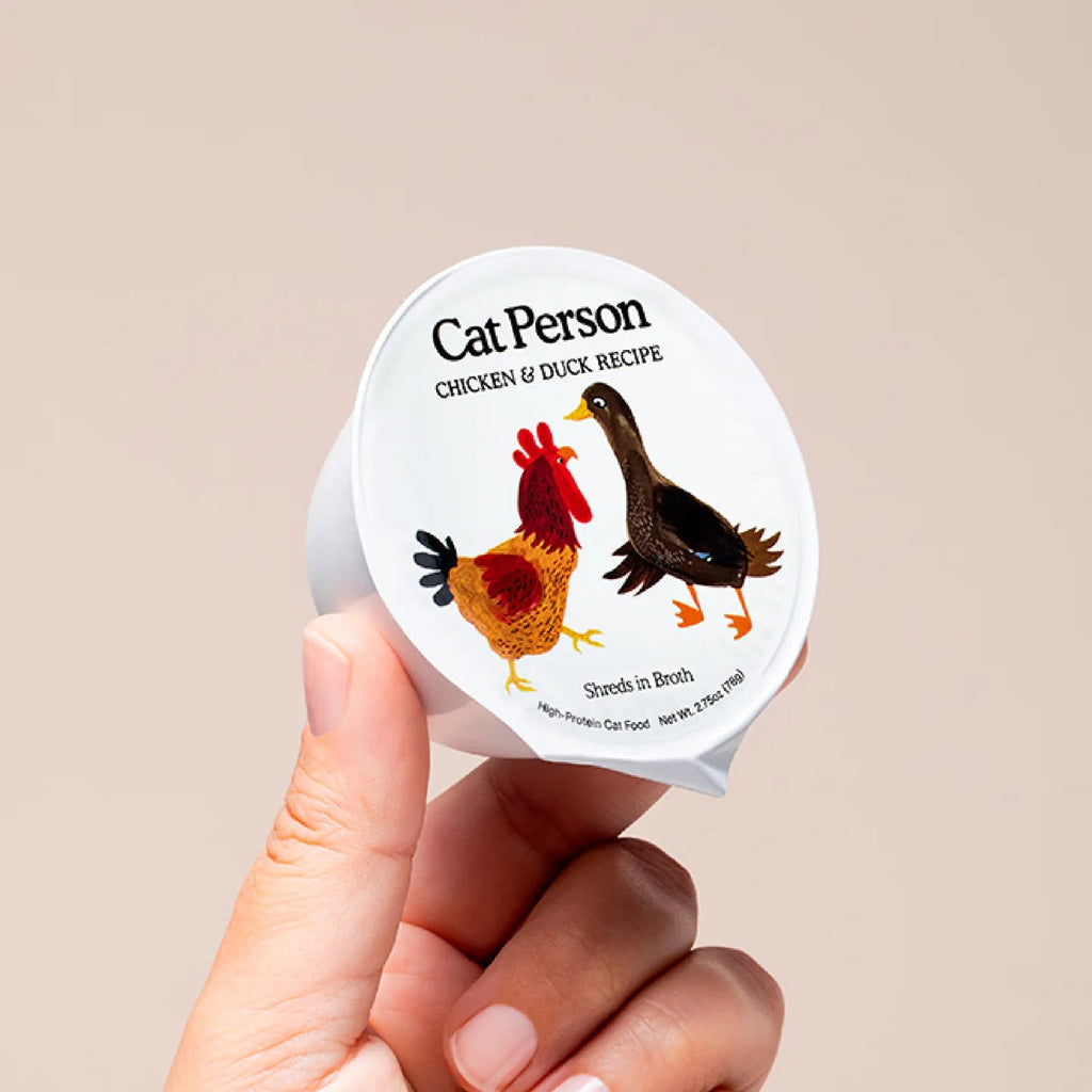 Cat Person cat food cup with chicken & duck illustration, shreds in broth, in hand