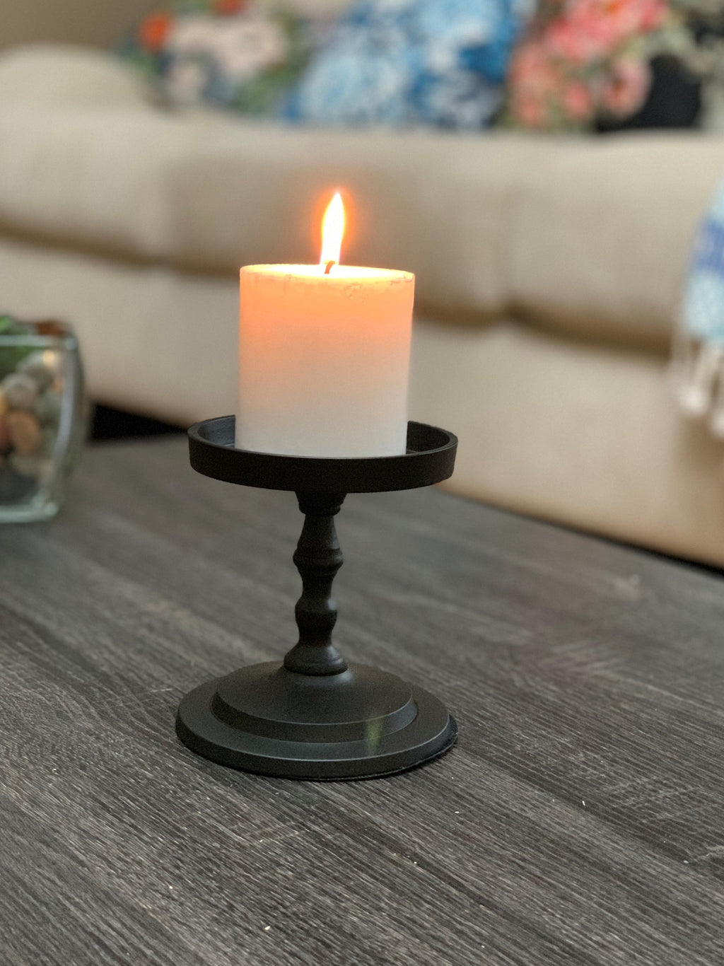Matte black pillar candle holder with lit white pillar candle on top tray