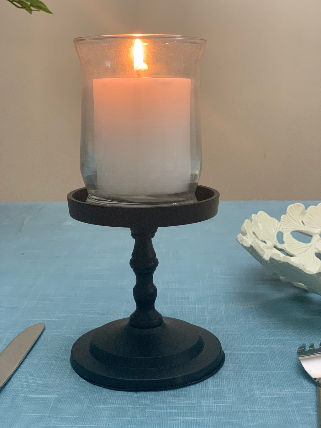 Matte black pillar candle holder with lit white candle inside clear glass