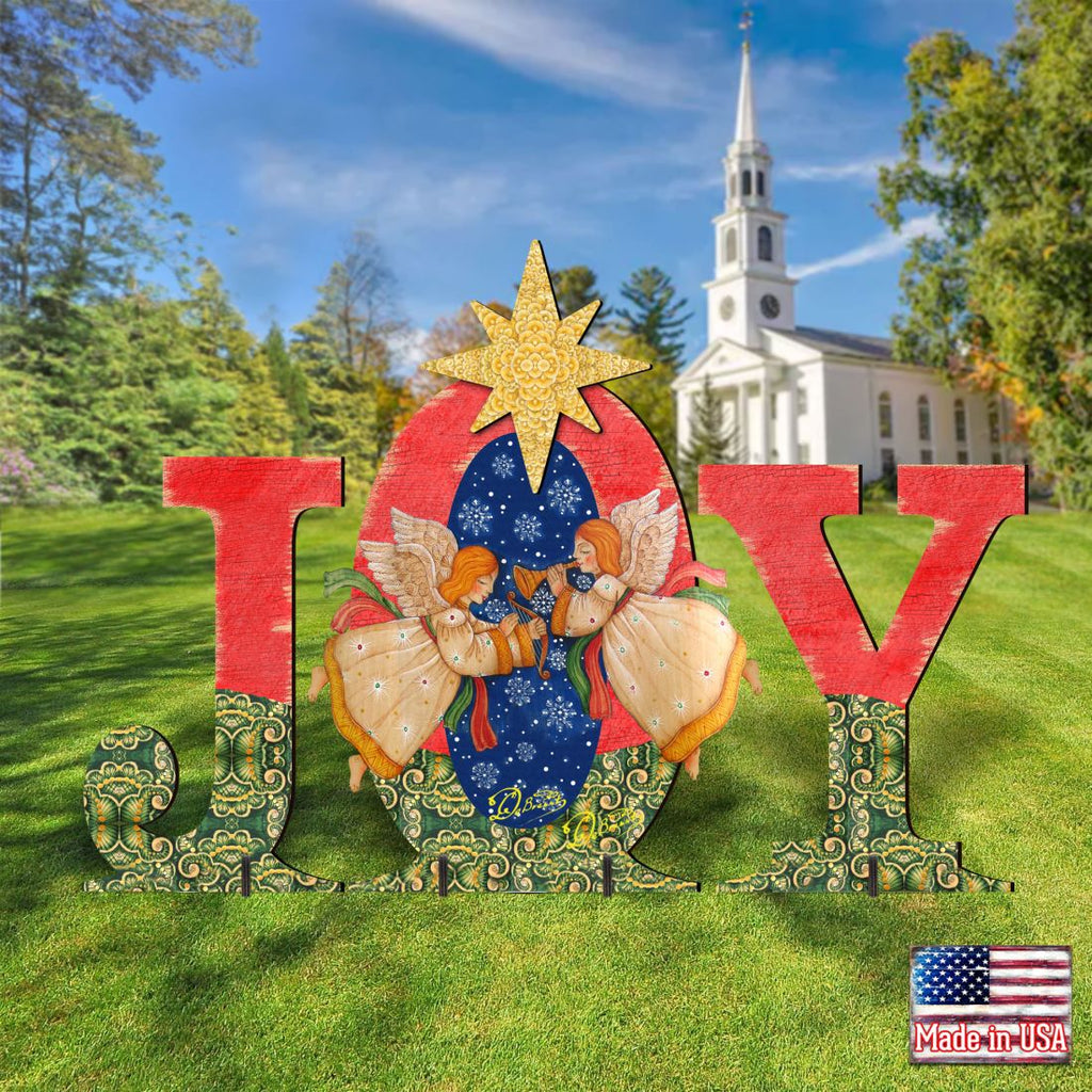 Outdoor “JOY” nativity yard decor with angels and yellow star in front of a white church.