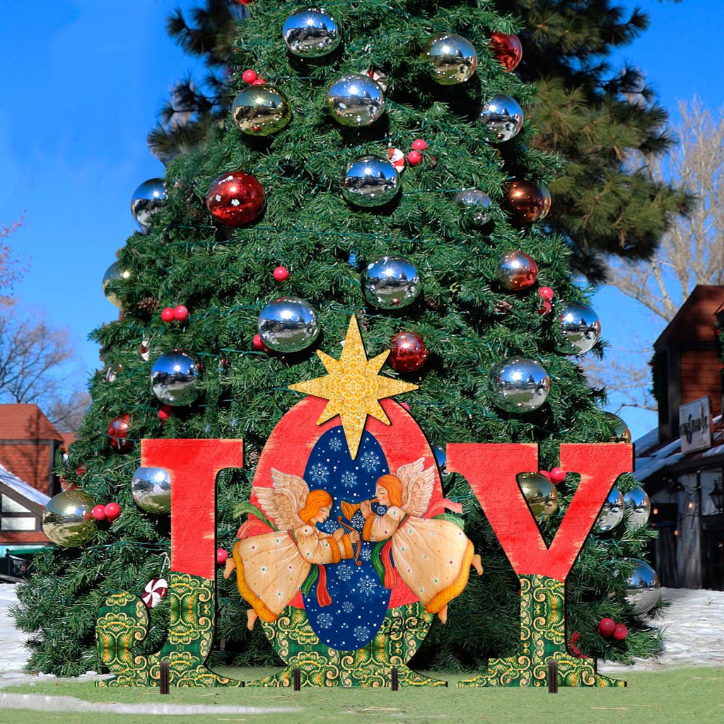 Outdoor “JOY” nativity yard decor with angels and yellow star in front of a decorated tree.