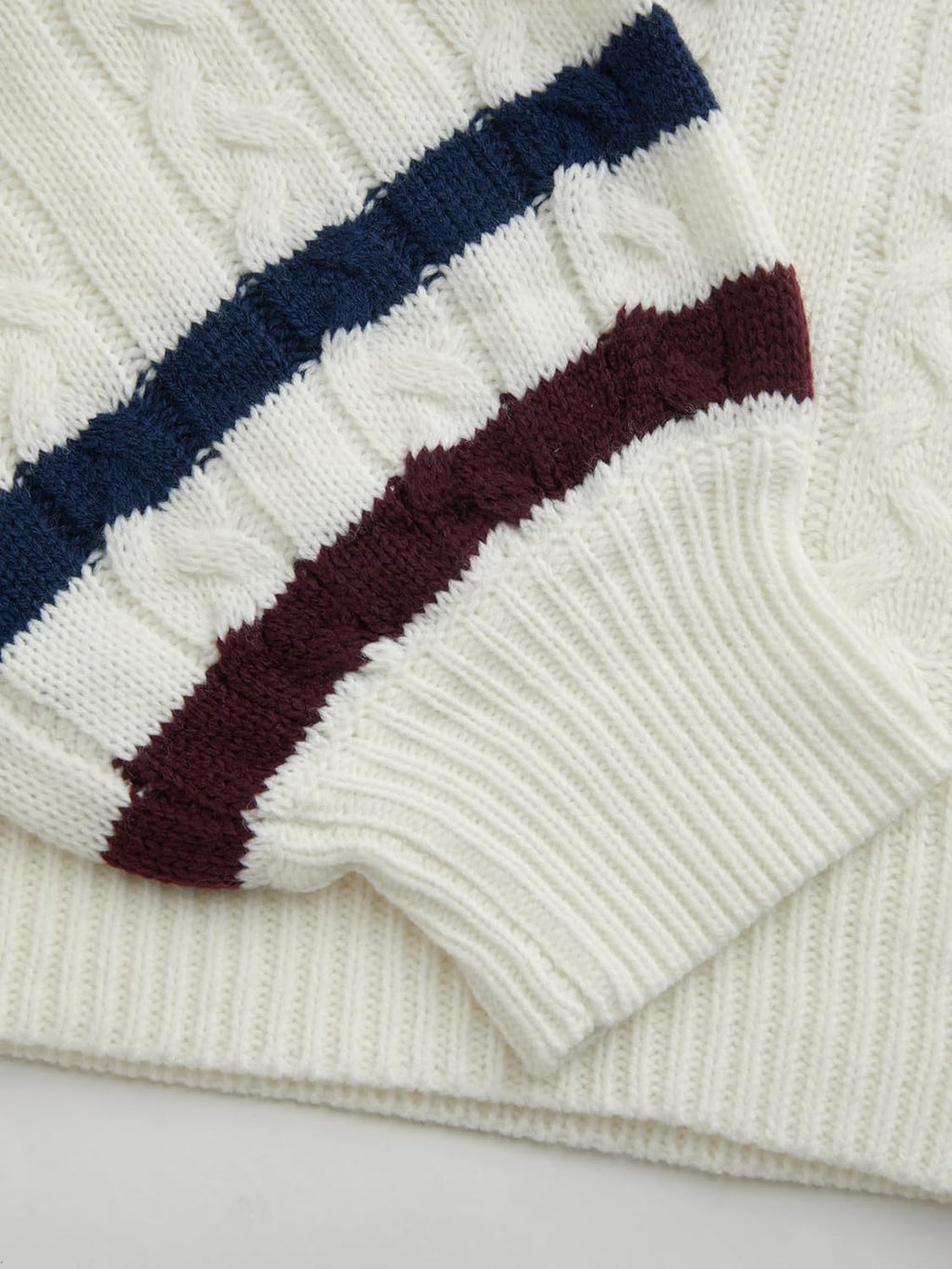 Folded cuff detail on cream cable-knit sweater with navy and wine stripe ribbing