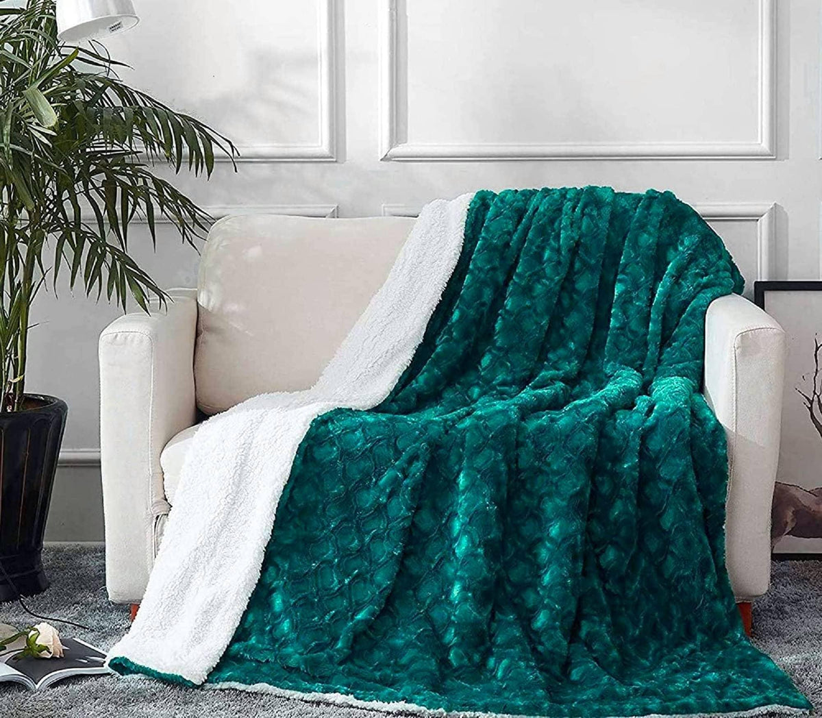 Faux fur sherpa throw blanket folded on a light sofa, dark teal plush with white backing