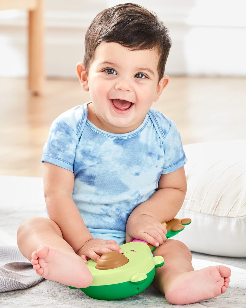 Baby holding green avocado guitar toy with brown tuning knobs, smiling