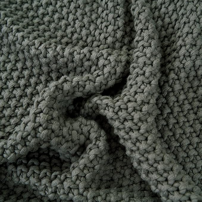 Close-up of chunky cable knit throw blanket texture in dark gray-green.