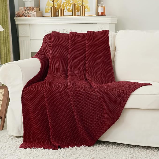 Wine red chunky cable-knit cotton throw blanket covering a couch cushion.