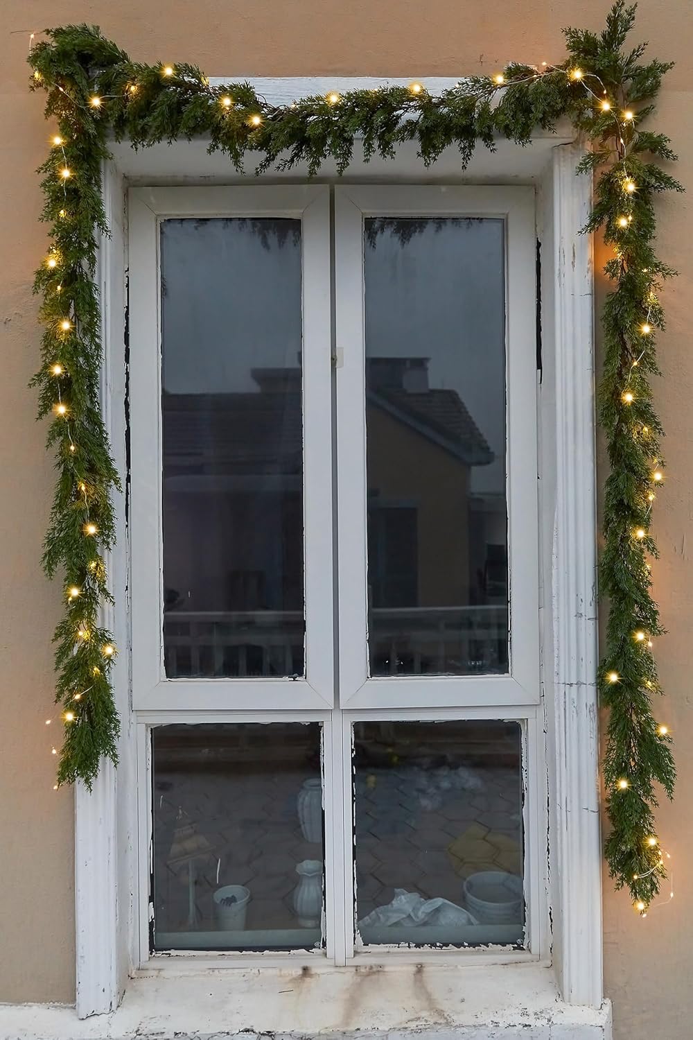 Artificial garland with warm LED lights hung across a window frame with greenery strands