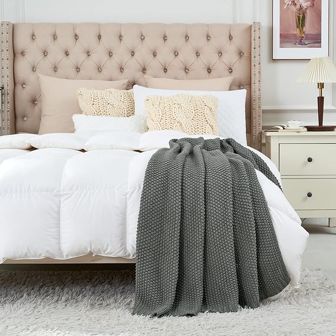 Chunky cable knit throw blanket in medium gray, loosely draped on a bed.