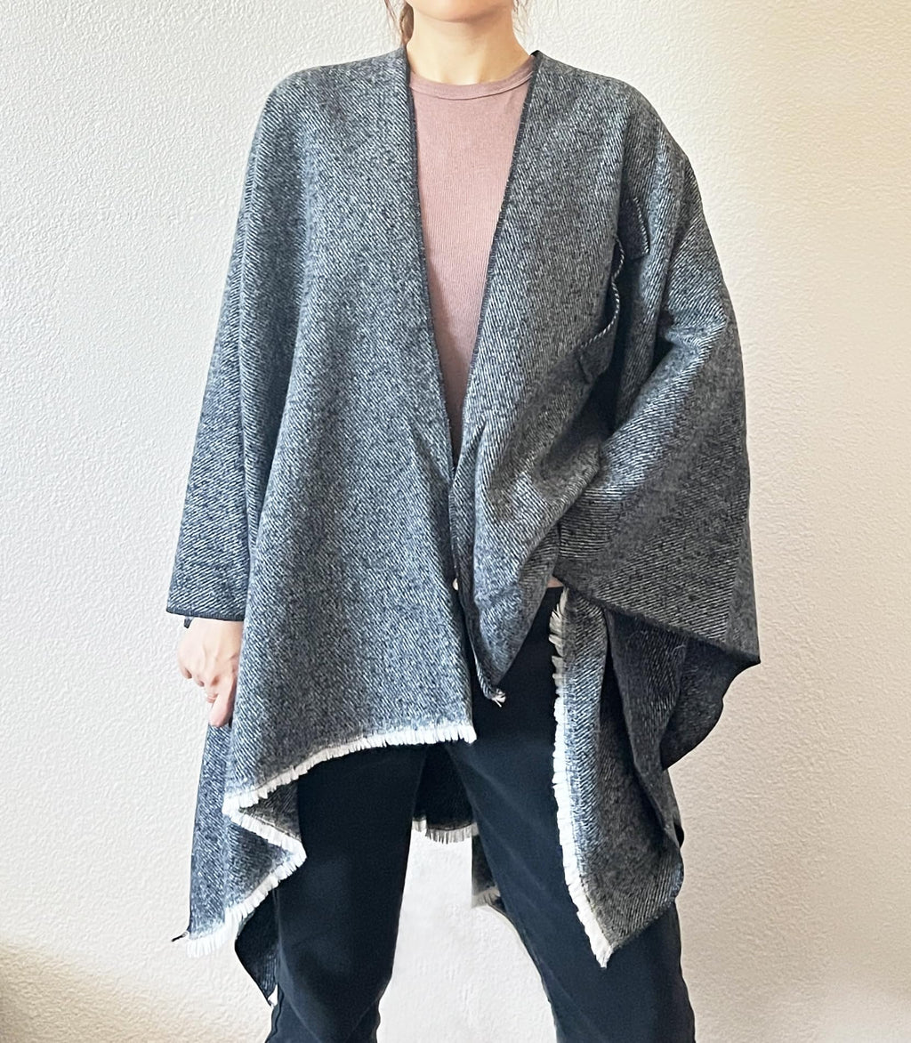Women’s blue-grey open-front fringe poncho shawl with V-neck opening and uneven hem trim.