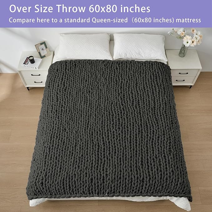 Dark grey oversized chunky knit throw blanket laid over bed, thick looped chenille texture.