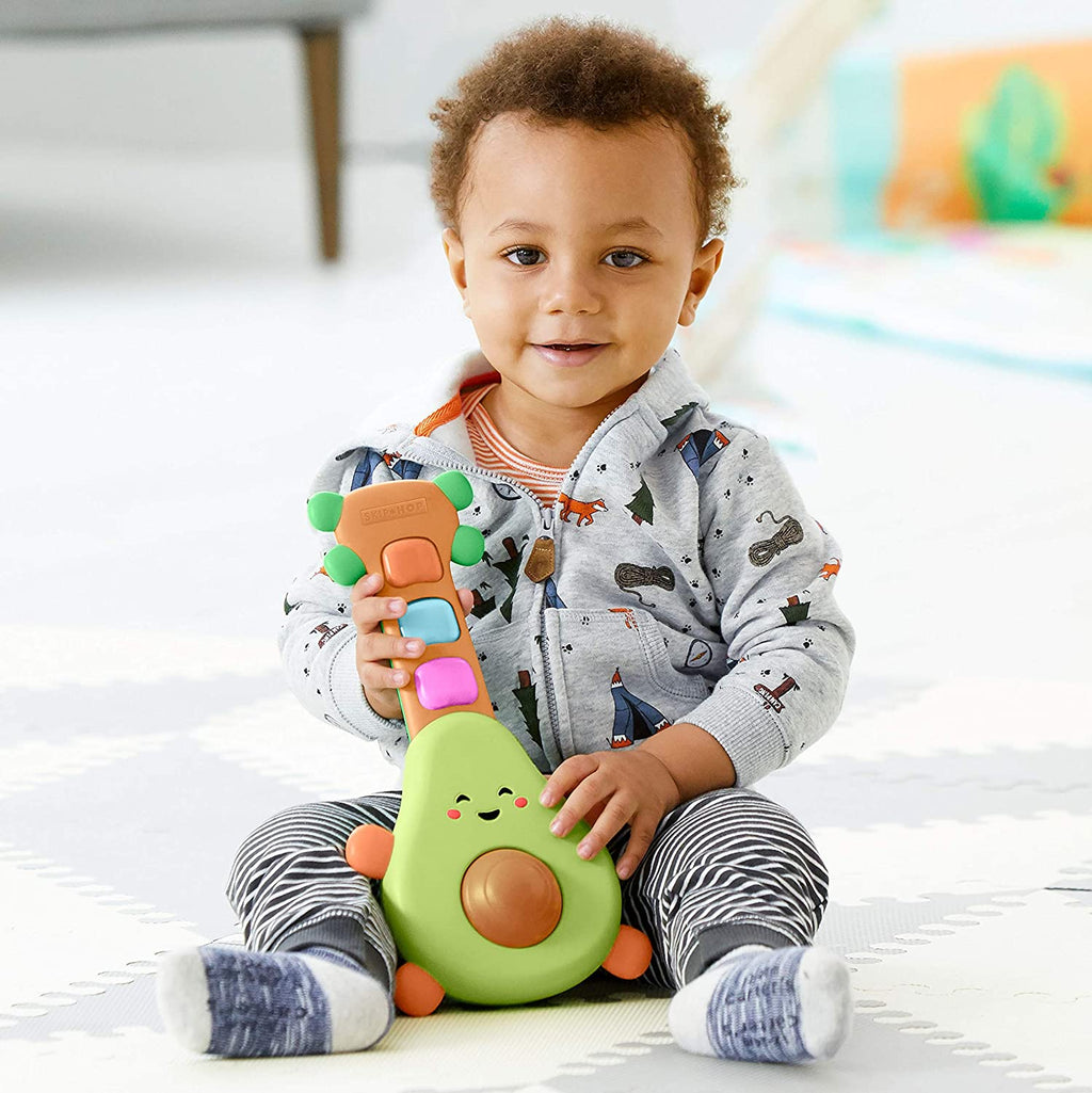 Toddler holding green avocado guitar toy with colorful button keys