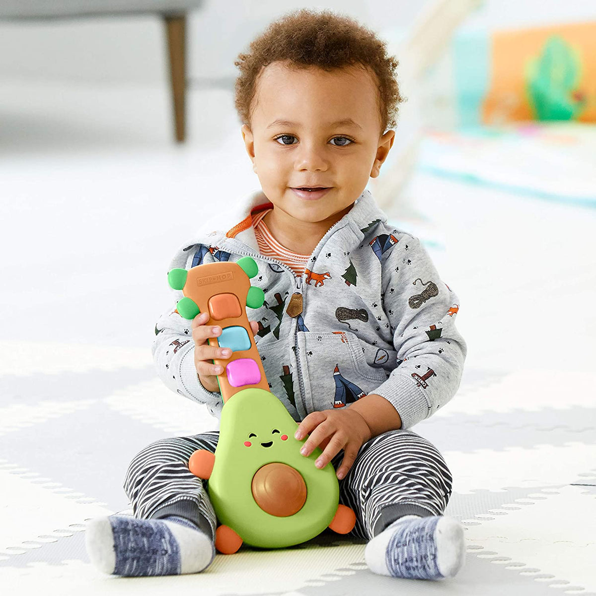 Toddler holding green avocado guitar toy with colorful button keys