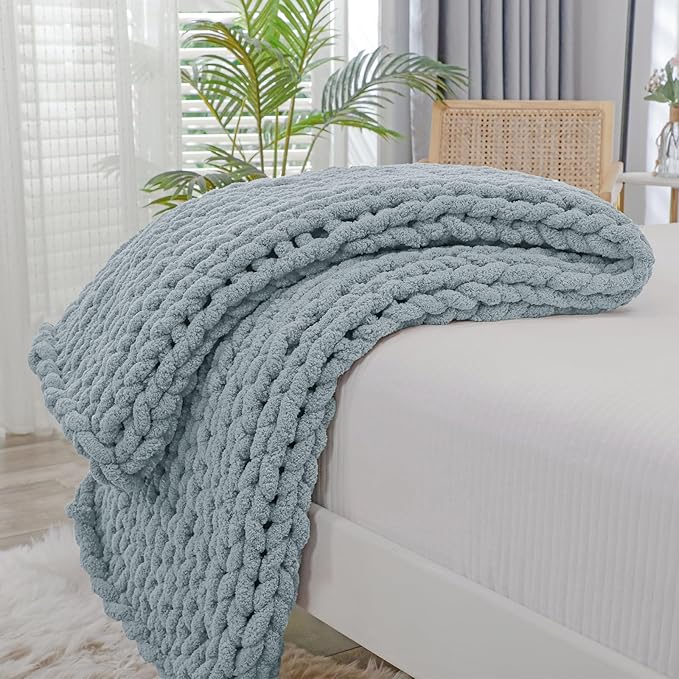 Dusty blue chunky knit throw blanket with rope-knot cable texture, folded on a sofa