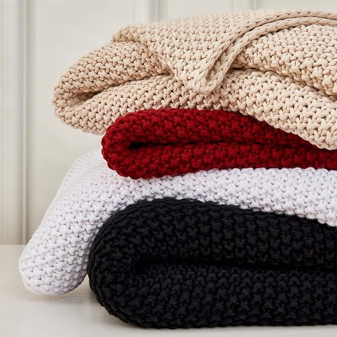 Stacked chunky knit throw blankets with wine red layer and cream and black layers.